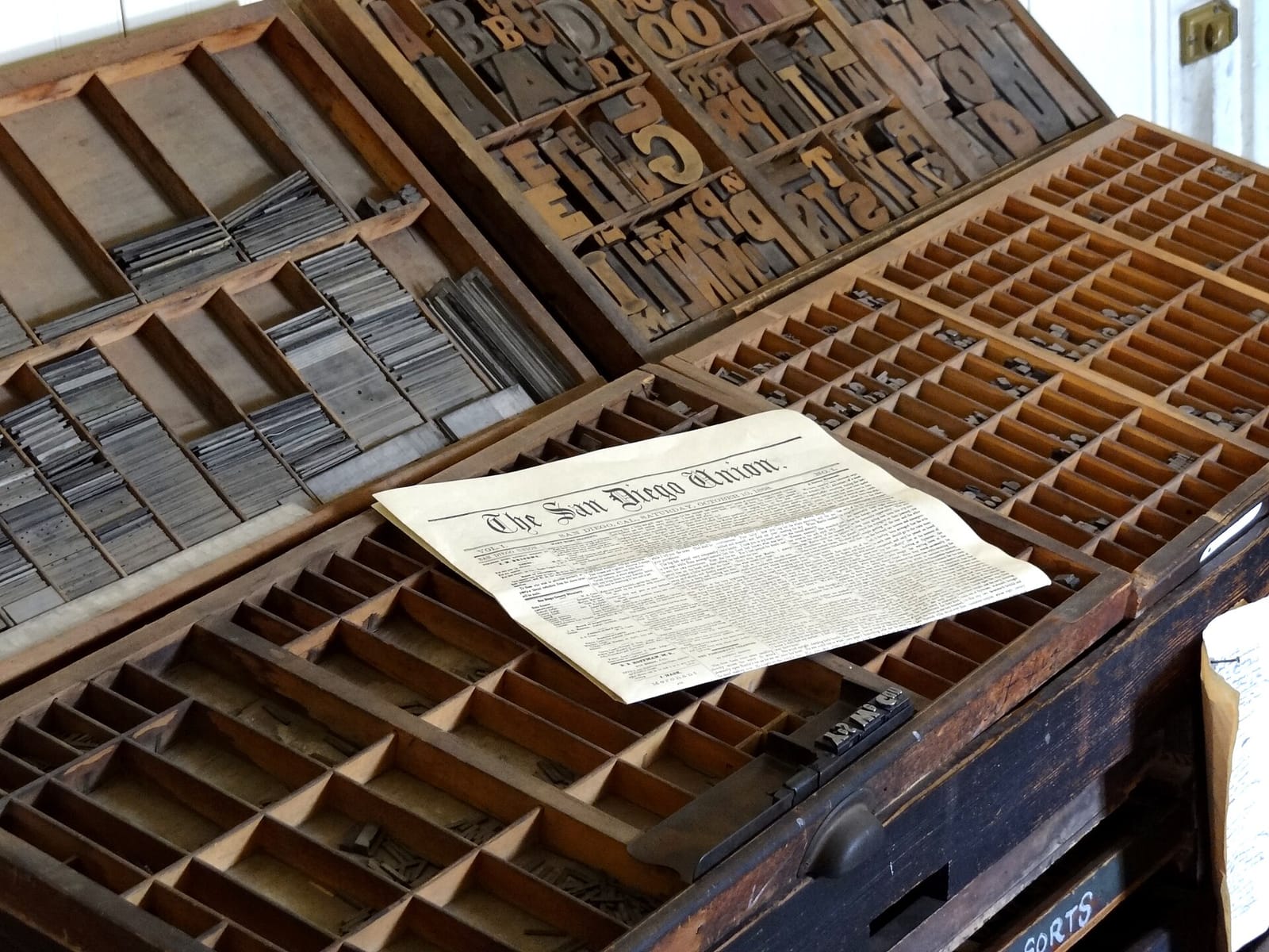 Una caja de tipos de imprenta antigua con un periódico encima